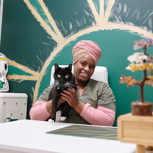 happy female wearing pink turban sitting behind desk and holding black and white cat happy female wearing pink turban sitting behind desk and holding black and white cat
