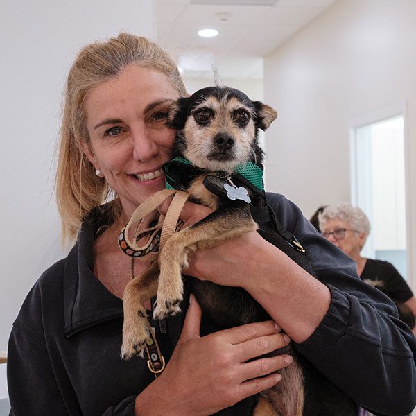female smiling while holding up small terrier dog